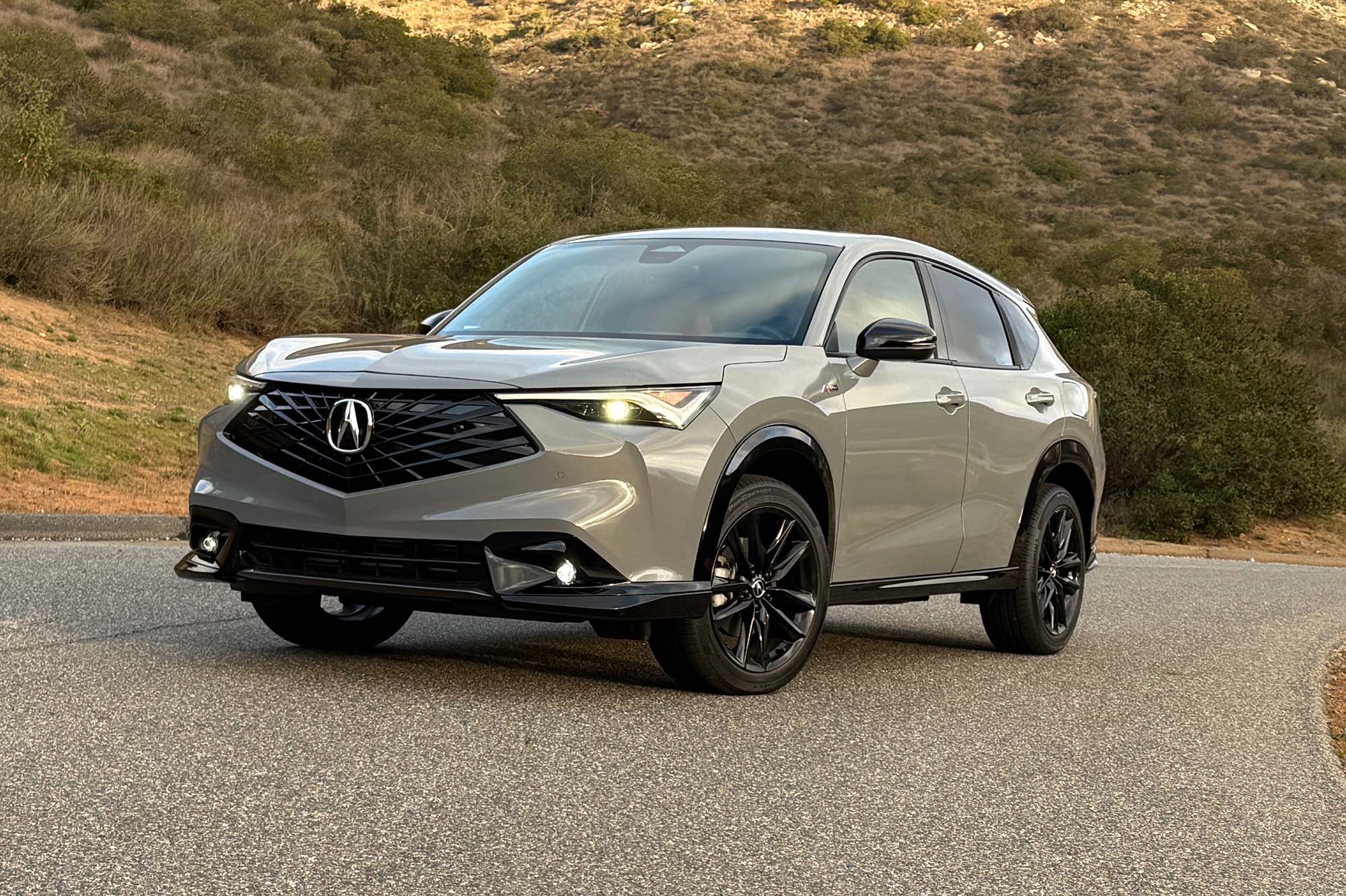 Front three-quarter view of a gray 2025 Acura ADX SUV parked on a paved road with hills.