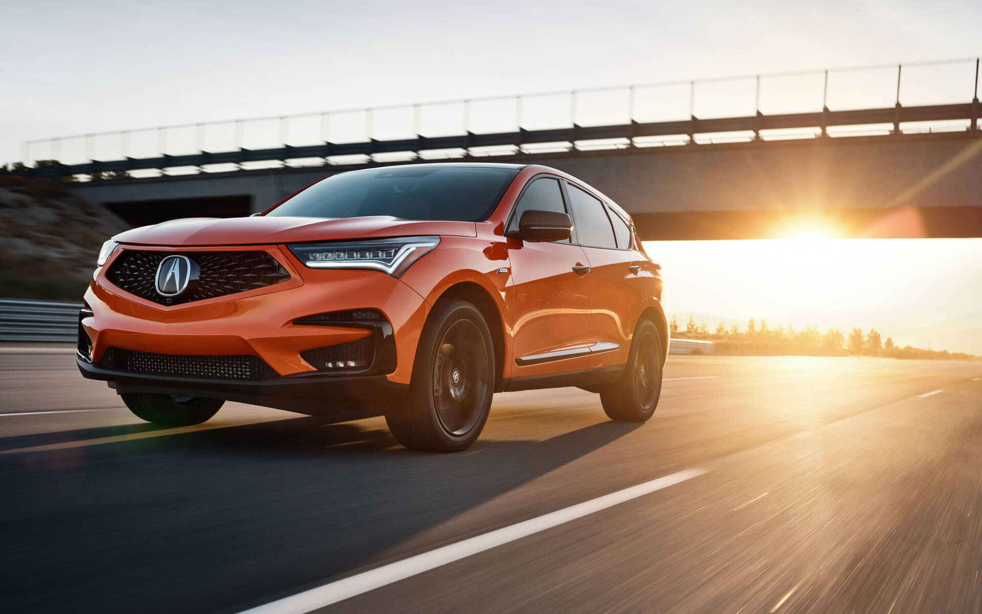 Front three-quarter view of an orange 2021 Acura RDX driving along a highway at sunset.