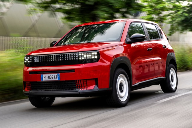 Red 2025 Fiat Grande Panda Electric hatchback traveling along a paved road with trees