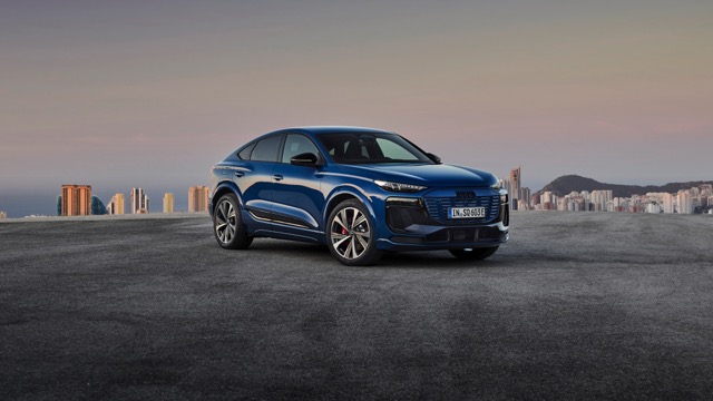 Front three-quarter view of a blue 2024 Audi SQ6 e-tron SUV parked outdoors with a city skyline.