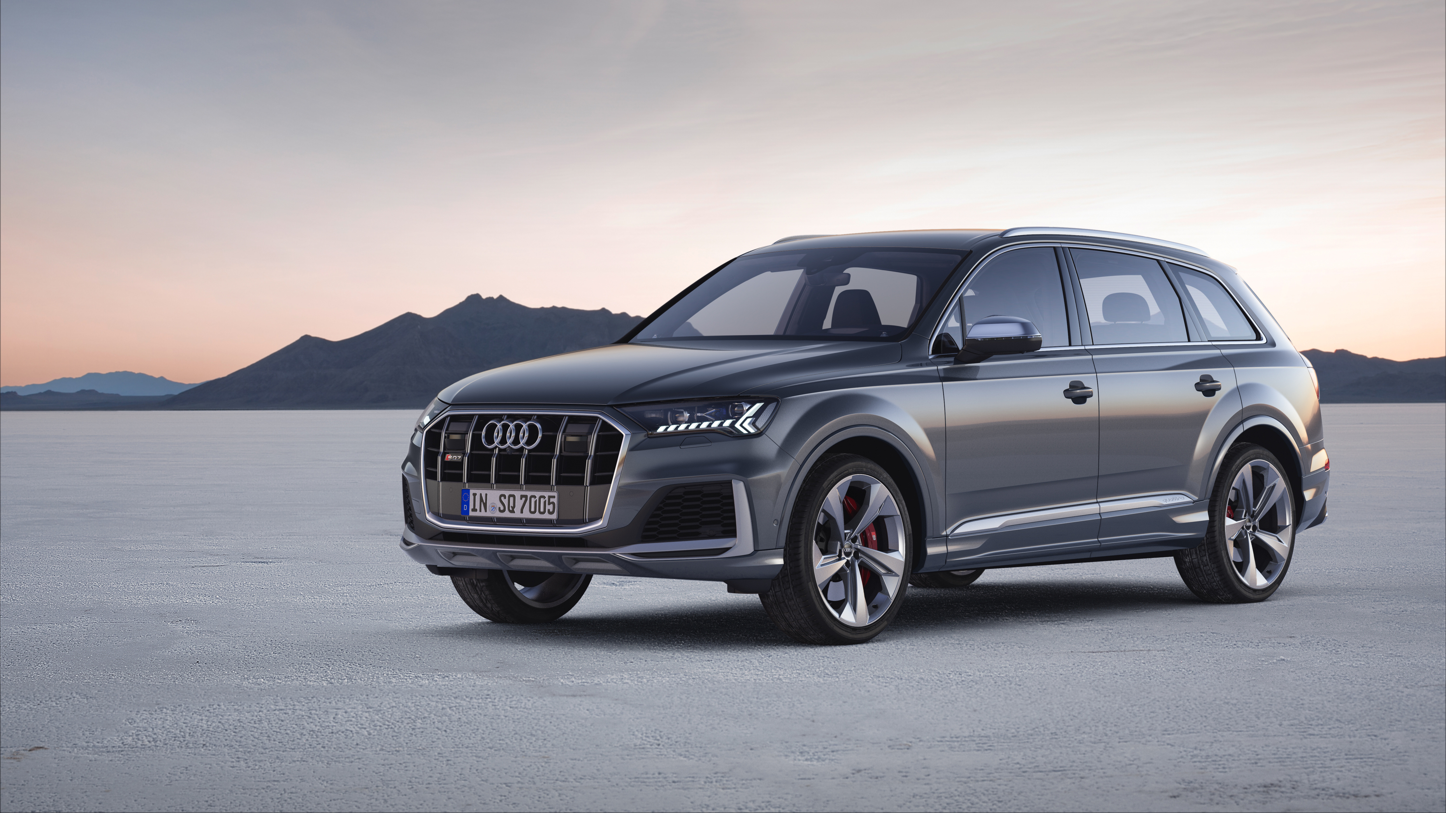 Front three-quarter view of a grey 2024 Audi Q7 SUV parked on an open desert landscape.