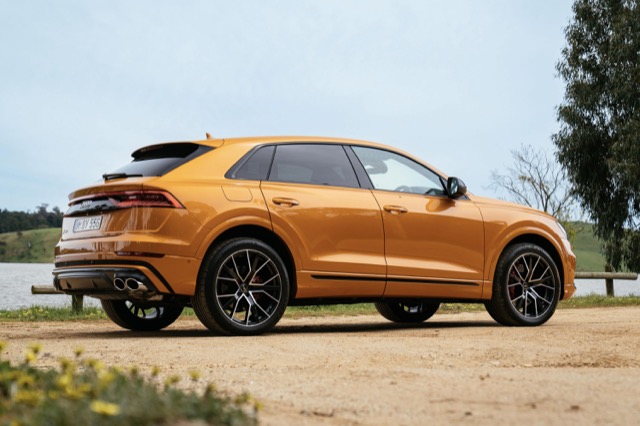 Rear three-quarter view of a gold 2023 Audi SQ8 parked on a dirt road outdoors.