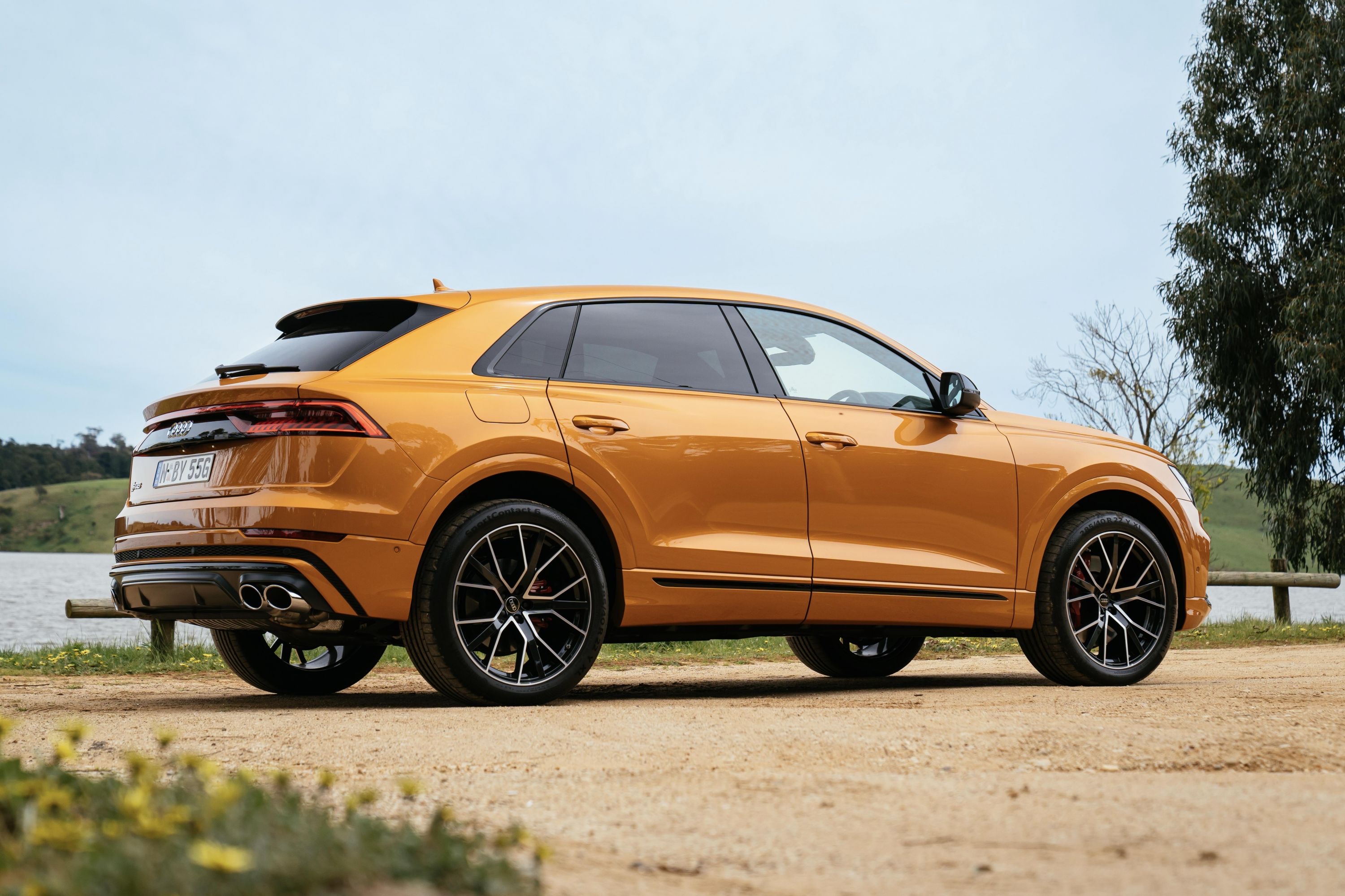 Rear three-quarter view of a gold 2023 Audi SQ8 parked on a dirt road outdoors.