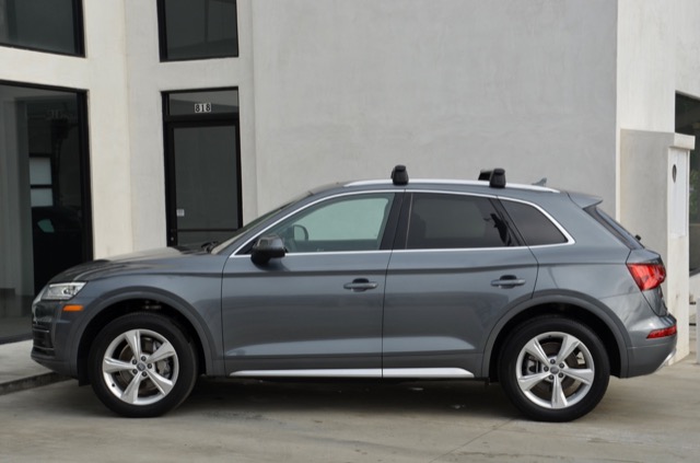 Side profile of a grey 2020 Audi Q5 SUV with roof rack crossbars parked outside a building