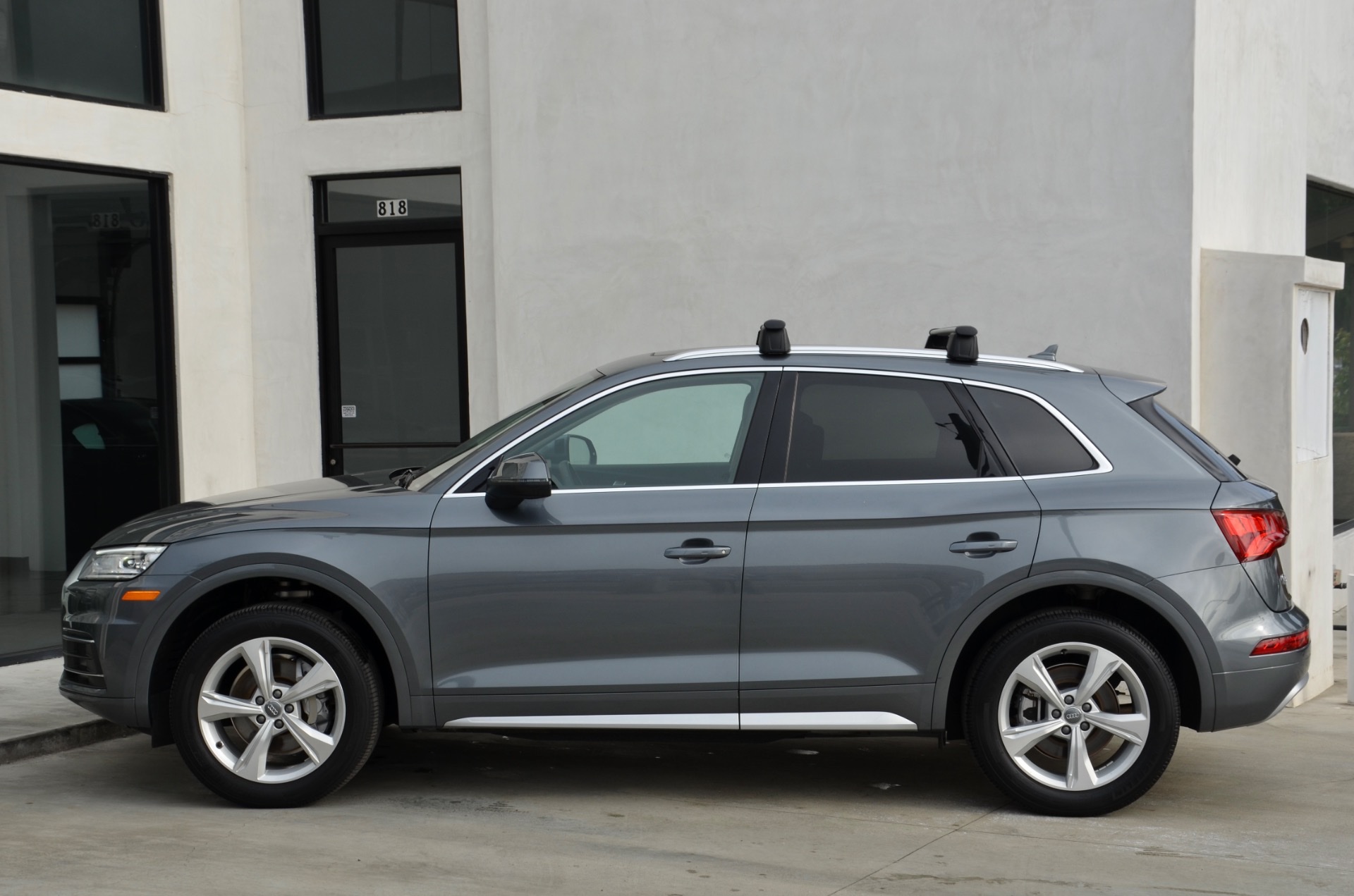 Side profile of a grey 2020 Audi Q5 SUV with roof rack crossbars parked outside a building