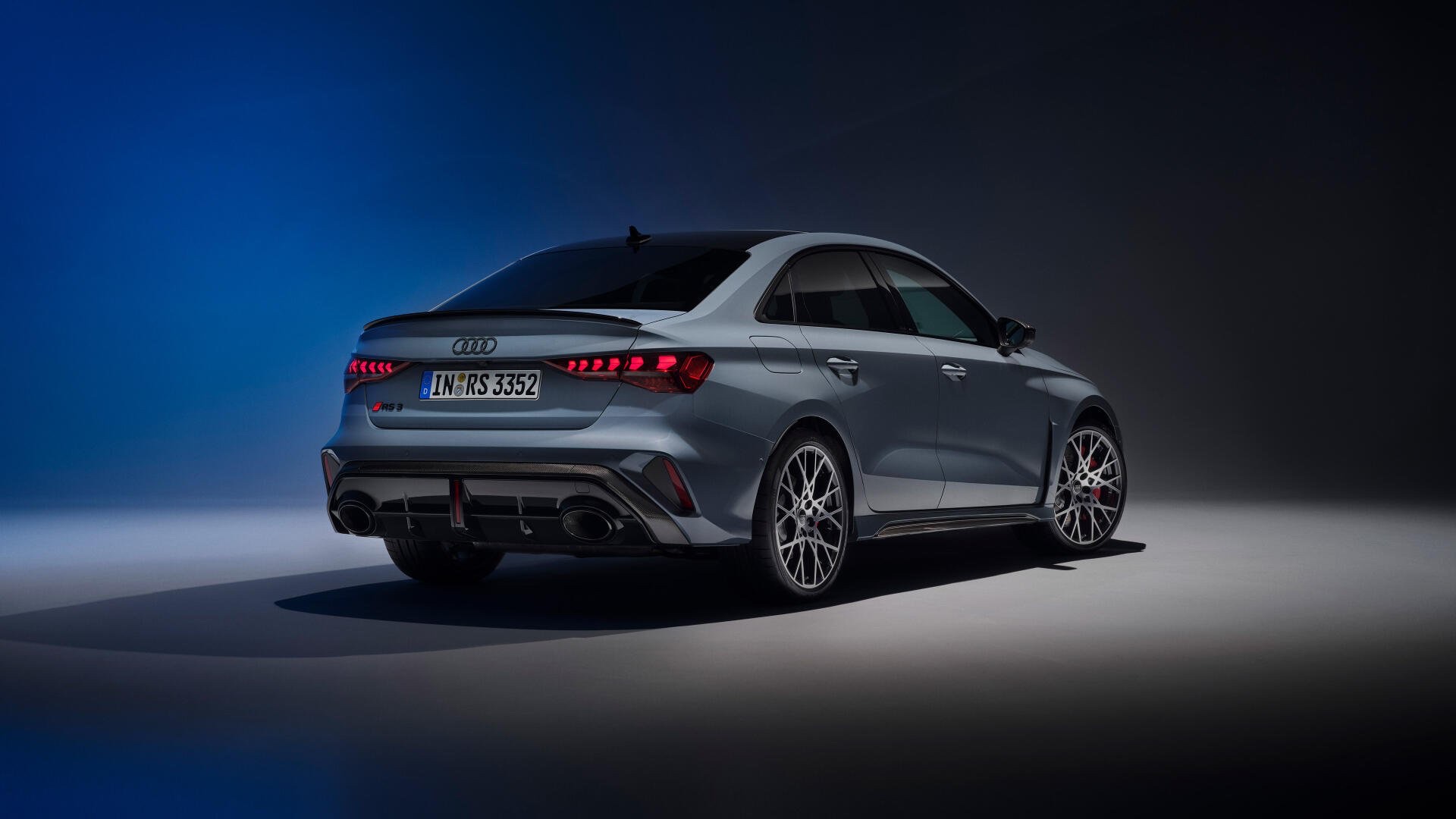 Rear three-quarter view of a grey 2021 Audi RS 3 Sedan in a dark studio setting
