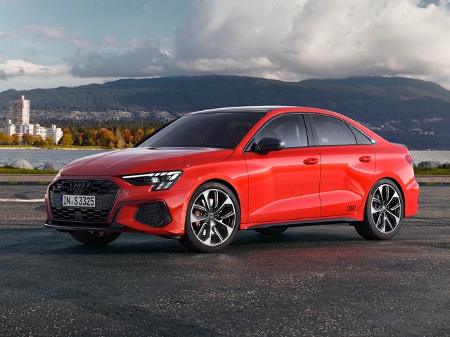 Front three-quarter view of a red Audi S3 Sedan parked outdoors with mountains in the background.