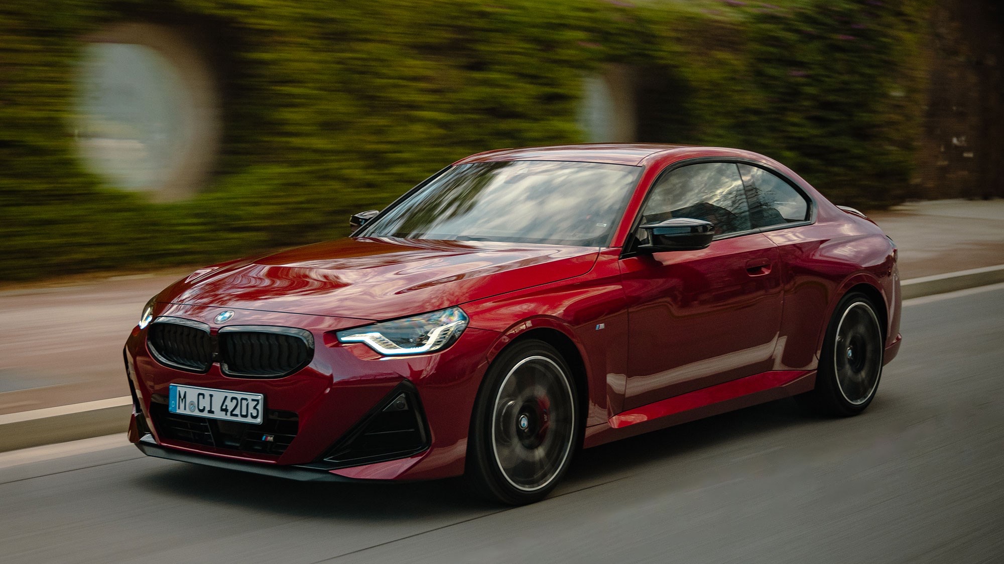 Front three-quarter view of a red 2021 BMW 2 Series Coupe driving along a paved road.