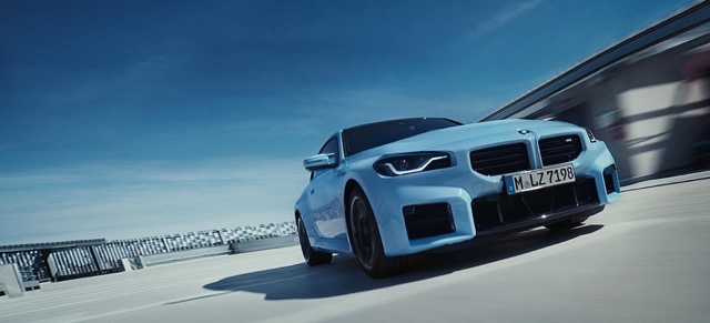 Low-angle front three-quarter view of a light blue 2022 BMW M2 Coupe on a paved rooftop structure.