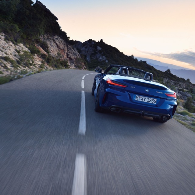 Rear three-quarter view of a blue 2022 BMW Z4 Roadster driving along a mountain road.