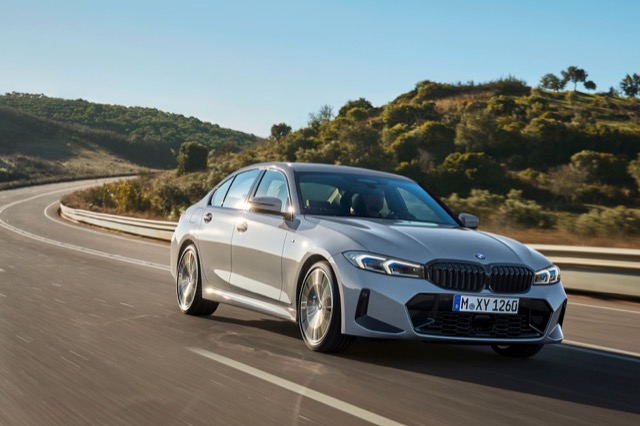 Front three-quarter view of a silver 2022 BMW 3 Series Sedan driving on a winding paved road.