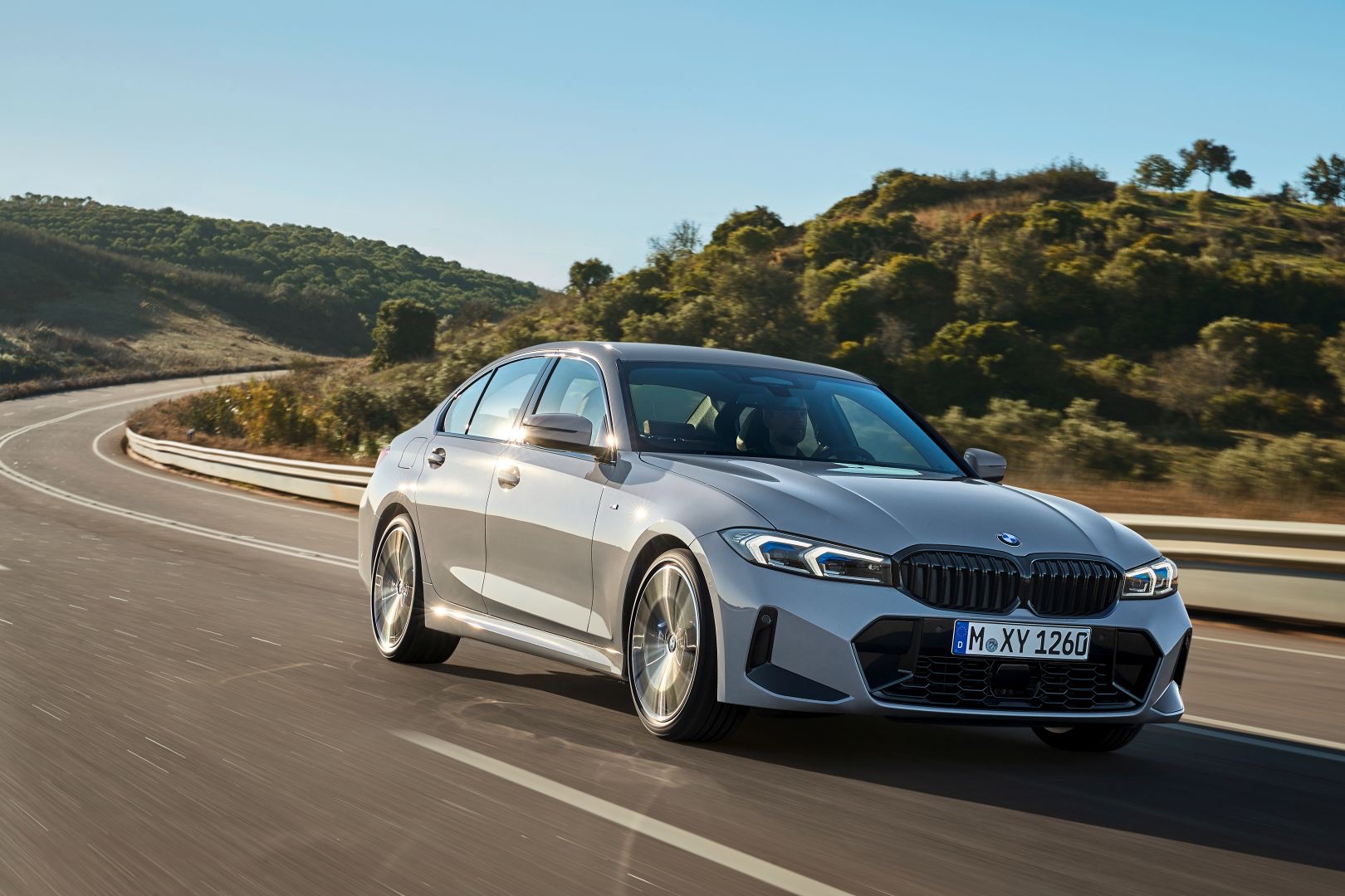 Front three-quarter view of a silver 2022 BMW 3 Series Sedan driving on a winding paved road.