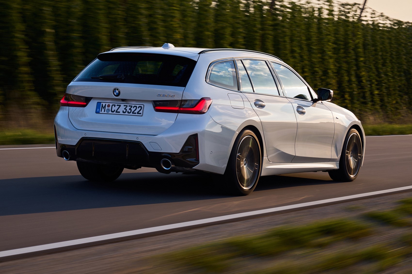 Rear three-quarter view of a white 2022 BMW 3 Series Touring driving on an open road.