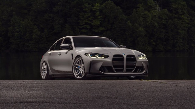 Grey 2020 BMW M3 Sedan shown in a front three-quarter view outdoors near trees and water.