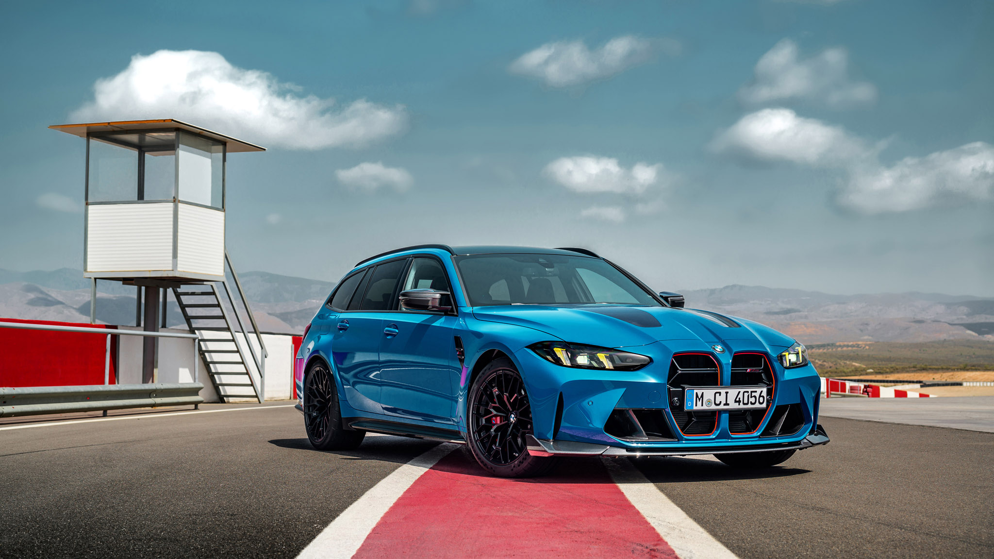 Front three-quarter view of a blue 2022 BMW M3 Touring wagon parked on a racetrack.