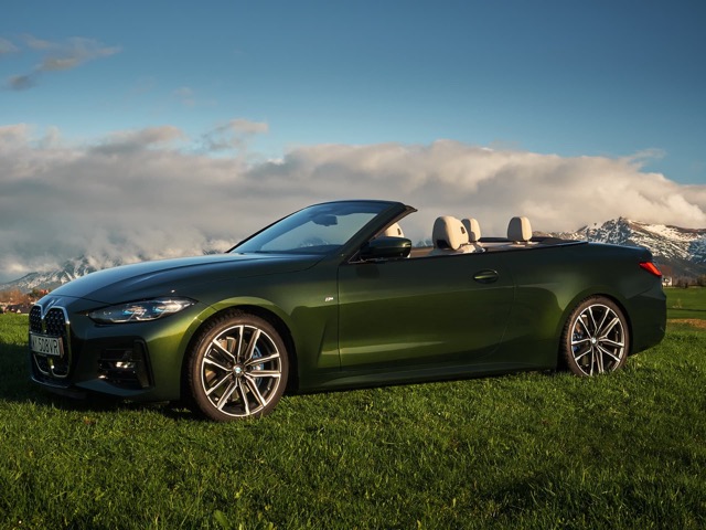 Side profile of a green 2020 BMW 4 Series Convertible parked on a grassy field.