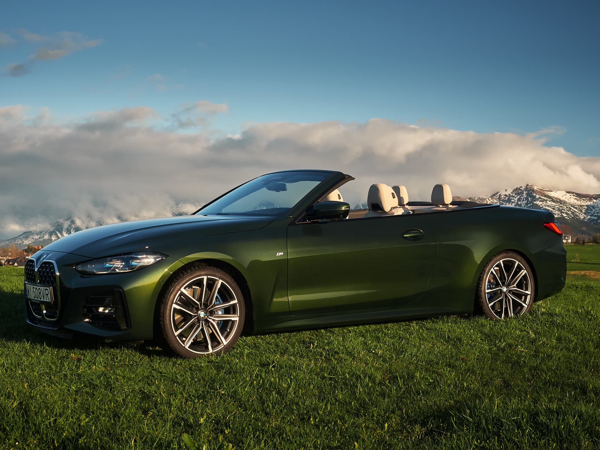 Side profile of a green 2020 BMW 4 Series Convertible parked on a grassy field.