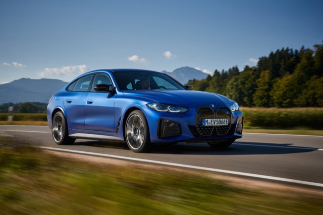 Front three-quarter view of a blue 2021 BMW i4 liftback driving on a paved road.