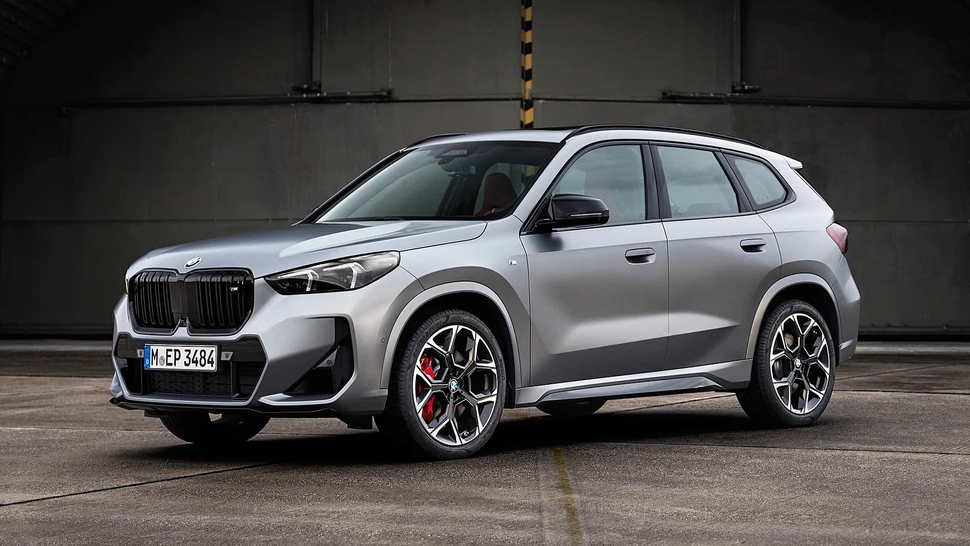 Three-quarter front view of a silver 2022 BMW X1 SUV parked outdoors in front of a structure.