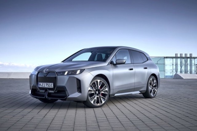Front three-quarter view of a silver 2025 BMW iX SUV parked on a paved outdoor surface.