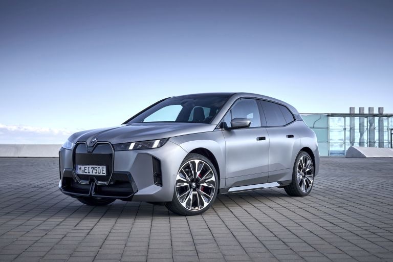 Front three-quarter view of a silver 2025 BMW iX SUV parked on a paved outdoor surface.