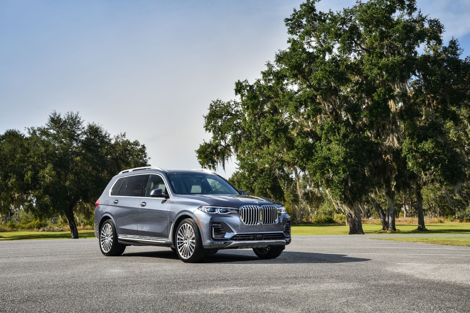 Front three-quarter view of a gray 2022 BMW X7 SUV parked on asphalt near trees.