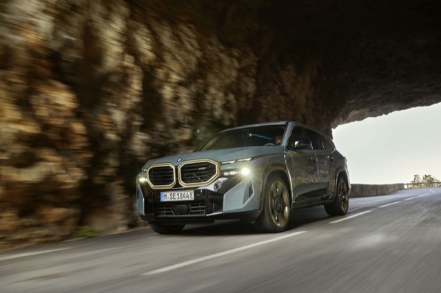 Front three-quarter profile of a grey 2022 BMW XM SUV driving along a paved mountain road.