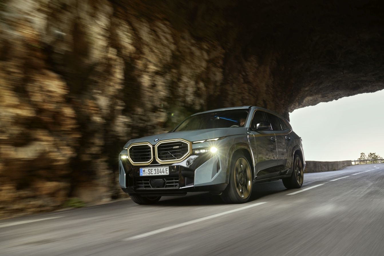 Front three-quarter profile of a grey 2022 BMW XM SUV driving along a paved mountain road.