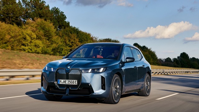 Front three-quarter view of a blue 2021 BMW iX SUV driving on an open road.
