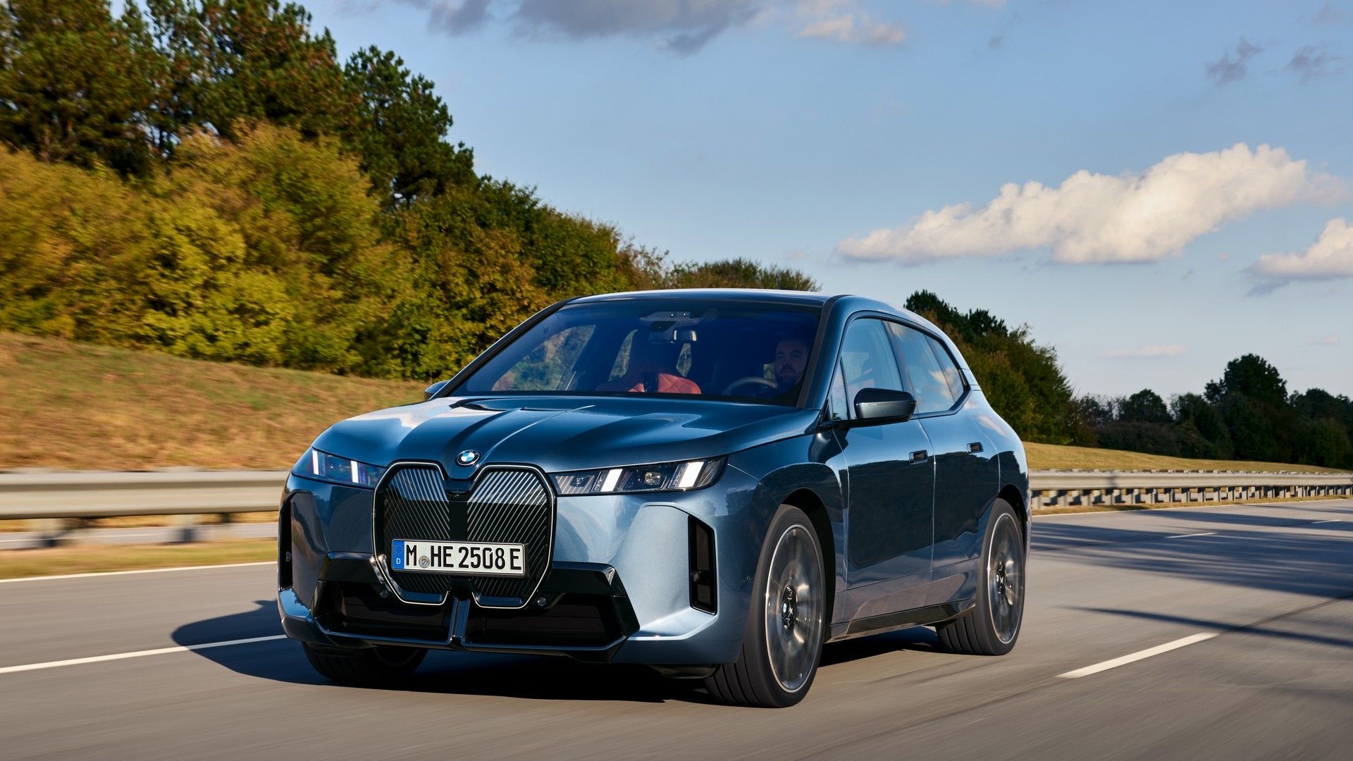 Front three-quarter view of a blue 2021 BMW iX SUV driving on an open road.