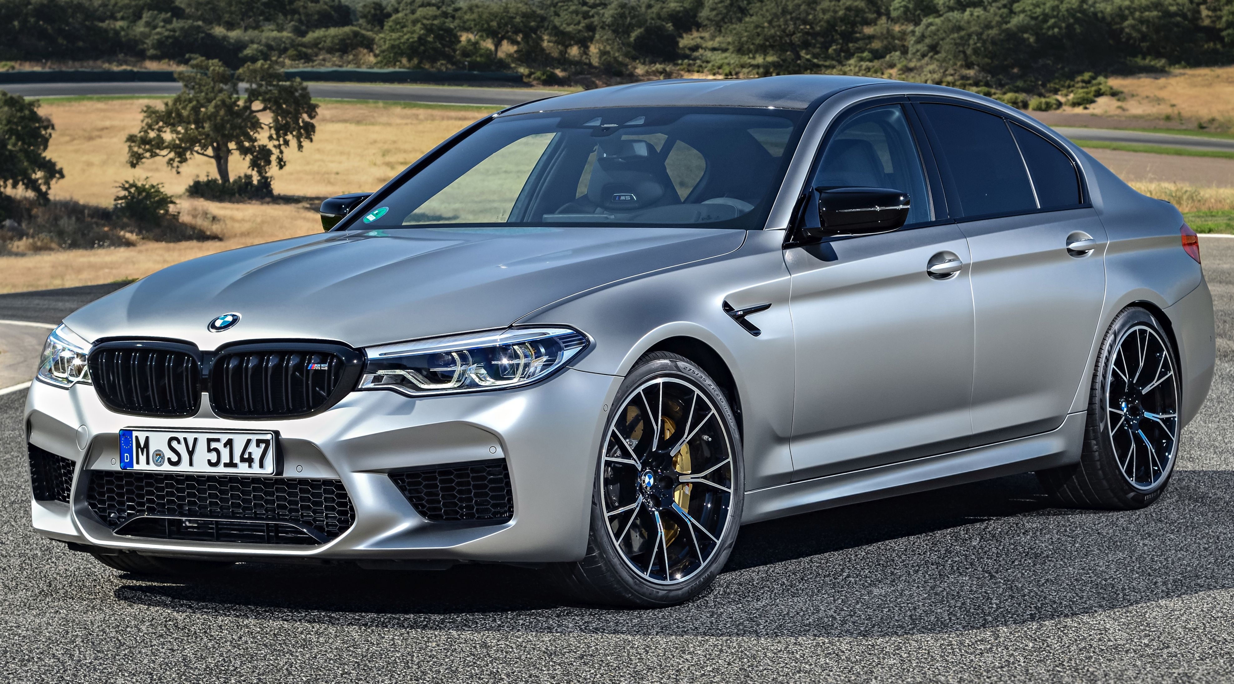 Front three-quarter view of a silver 2020 BMW M5 Sedan on an open asphalt track.