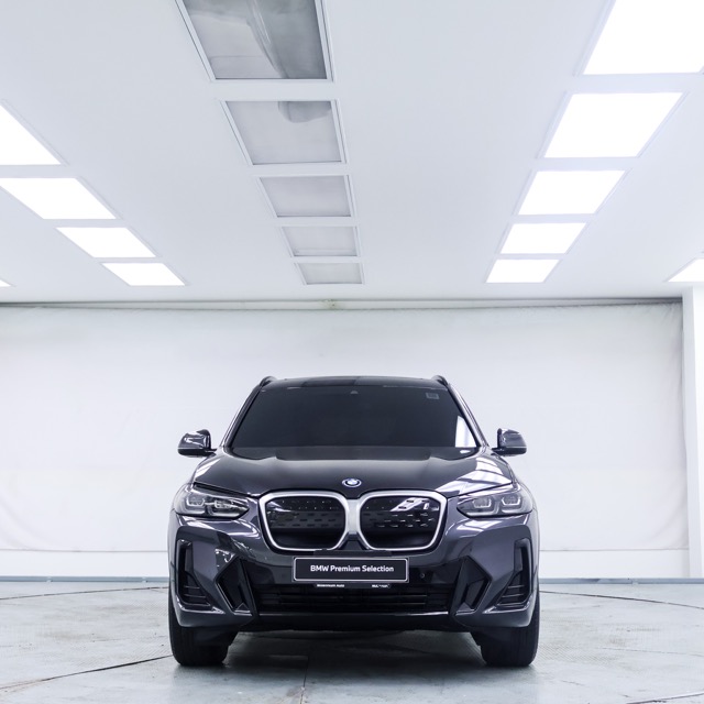 Front view of a dark grey 2021 BMW iX3 SUV parked in a brightly lit indoor showroom.