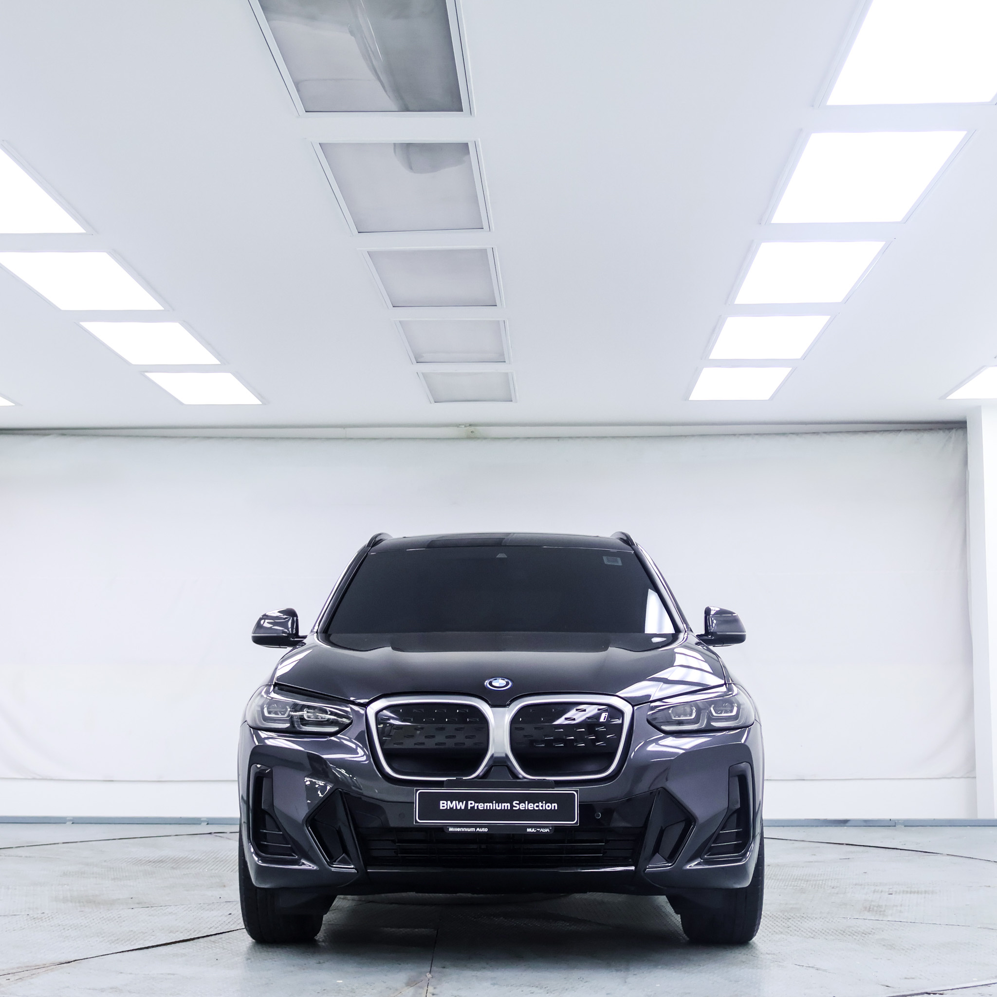 Front view of a dark grey 2021 BMW iX3 SUV parked in a brightly lit indoor showroom.
