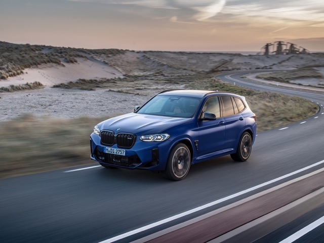 Front three-quarter view of a blue 2021 BMW X3 M driving on a coastal road.