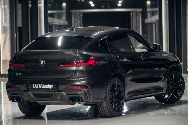 Rear three-quarter profile of a black 2021 BMW X4 SUV in an indoor space