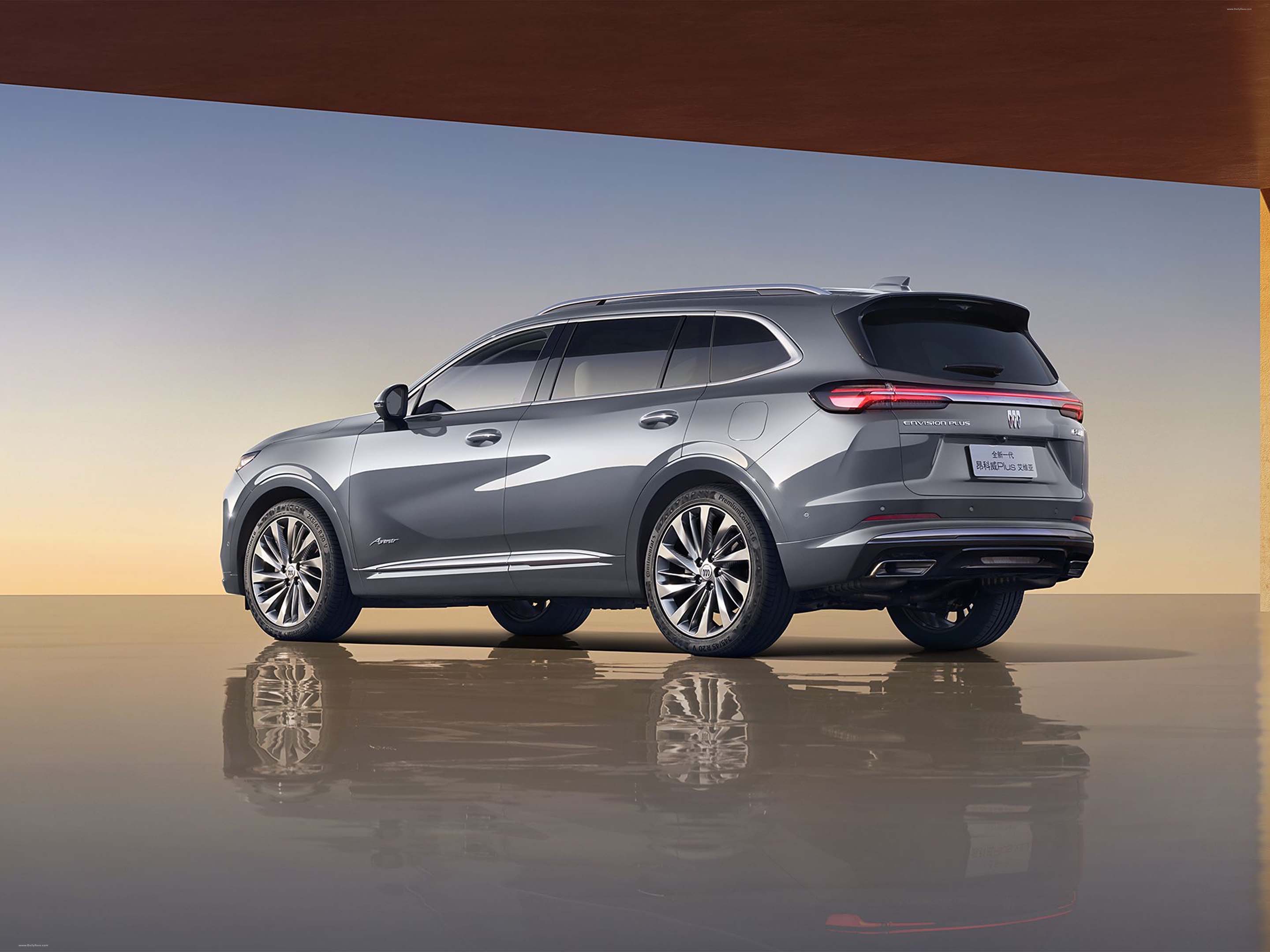 Rear three-quarter view of a grey 2024 Buick Envision SUV parked on a reflective studio surface.